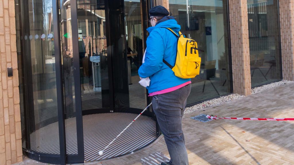 Iemand met een taststok loopt het gemeentehuis binnen