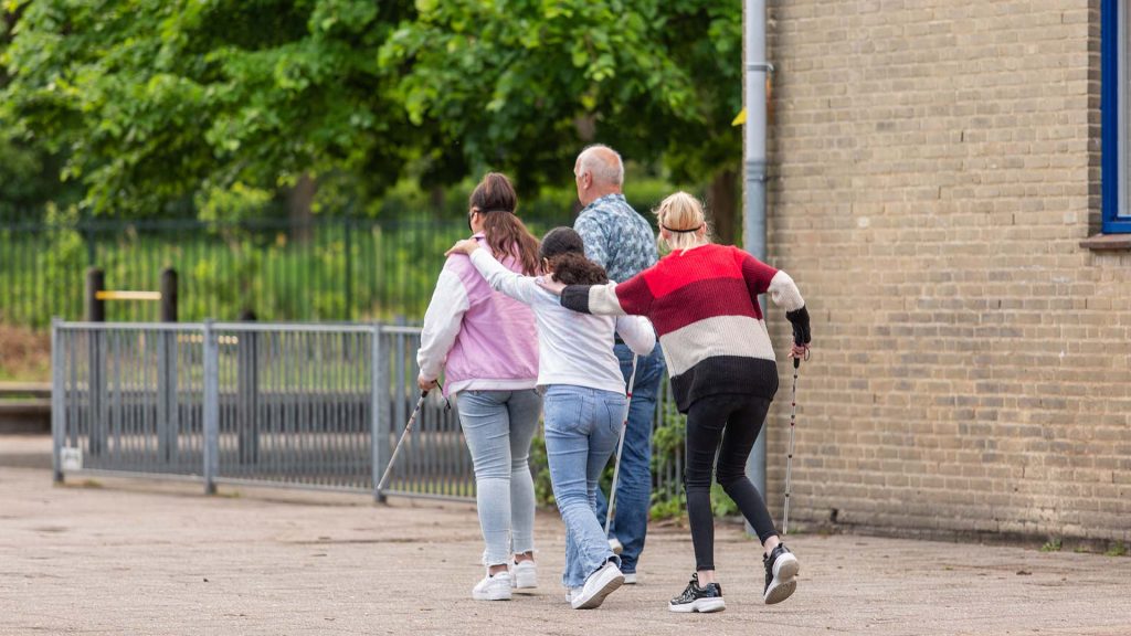 Drie meiden achter elkaar over het schoolplein met blinddoek en taststok.