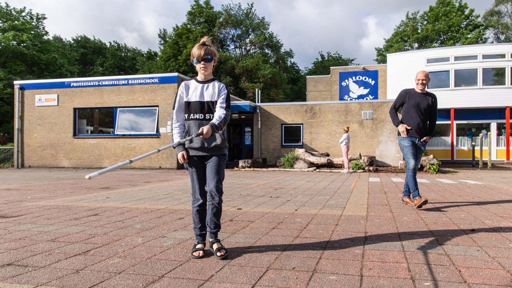 Een jongen uit groep 8 met een taststok op het schoolplein