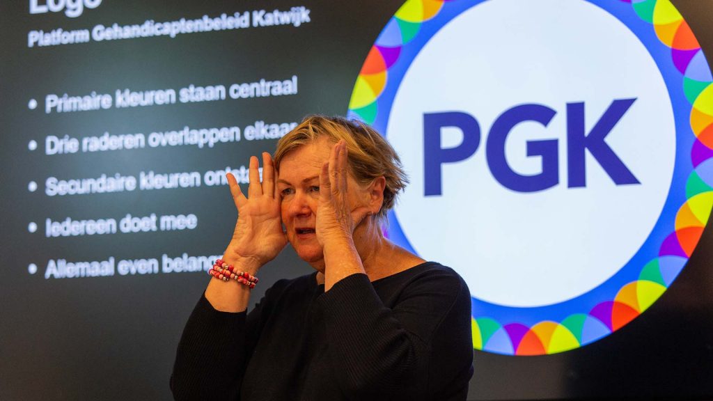 Vrijwilliger Marijke met op de achtergrond het logo van het platform Gehandicaptenbeleid Katwijk