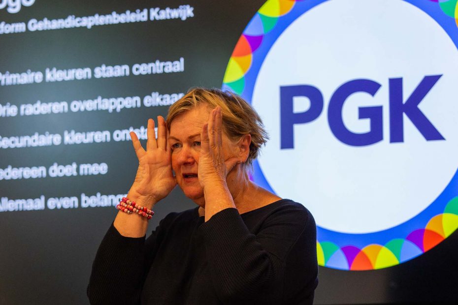 Vrijwilliger Marijke met op de achtergrond het logo van het platform Gehandicaptenbeleid Katwijk