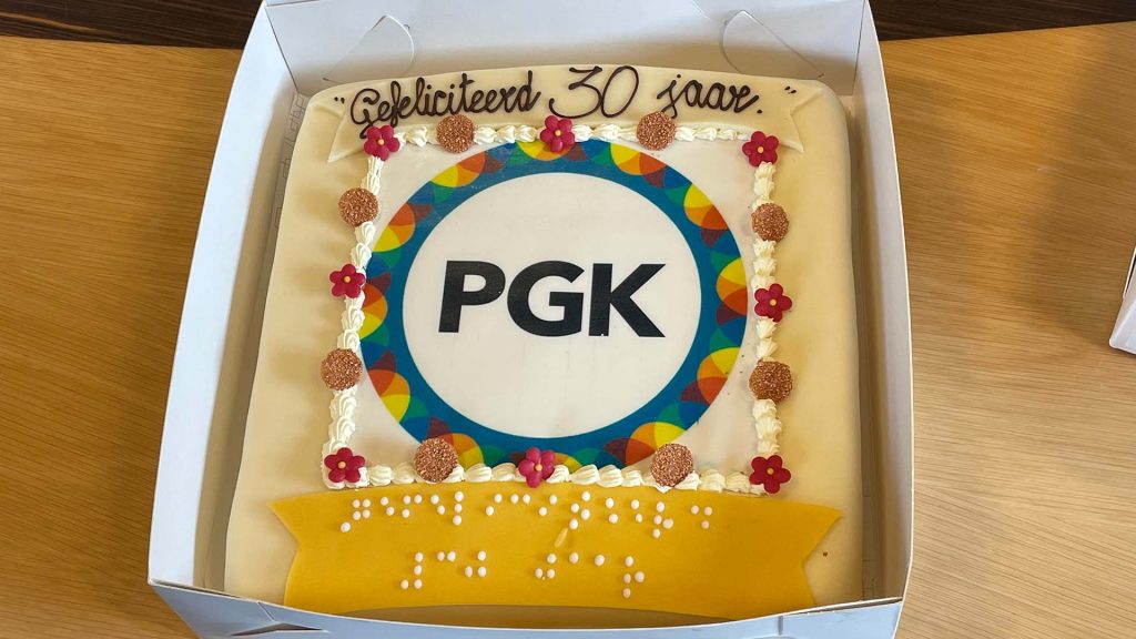 Een heerlijke taart met het logo van PGK en de felicitaties ook in brailleschrift.