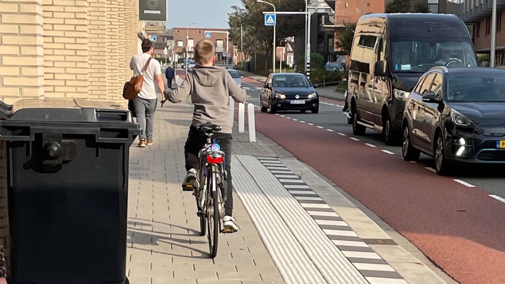 Een jongen fietst op de stoep naast de geleidelijn bij de bushalte naast de Action.