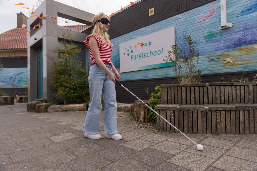 Een leerling met een taststok over het schoolplein 